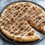 Cinnamon Dessert Pizza Recipe: A Sweet, Cozy Treat for Any Season 2 Close-up of a cinnamon dessert pizza with crumble topping and vanilla glaze drizzle on a pizza pan.