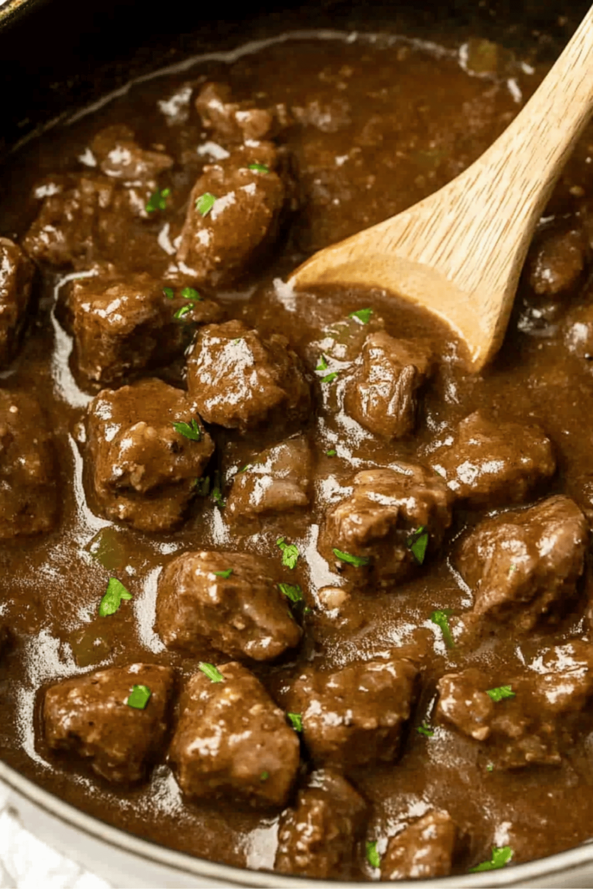 Beef Tips Simmering in Skillet Beef tips simmering in brown gravy inside a skillet with a wooden spoon.