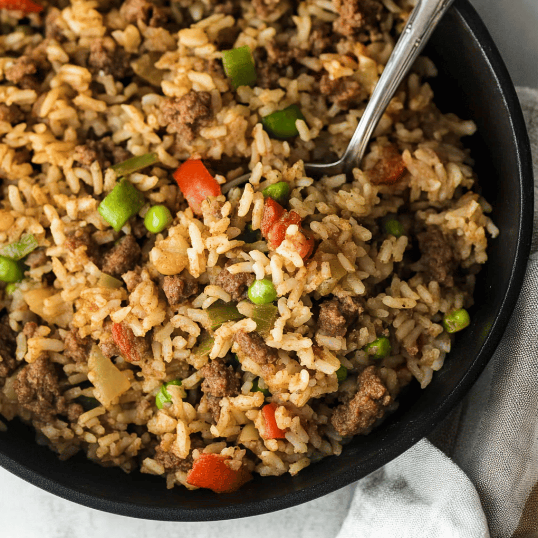 Dirty Rice with Peas, Peppers, and Ground Beef Bowl of dirty rice with ground beef, green peas, red bell peppers, and a spoon.