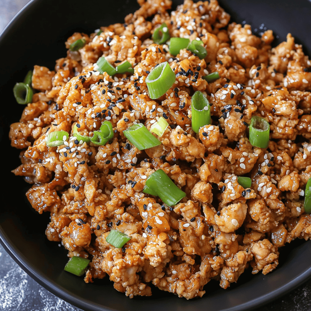 Bowl of sesame ground chicken garnished with green onions and sesame seeds