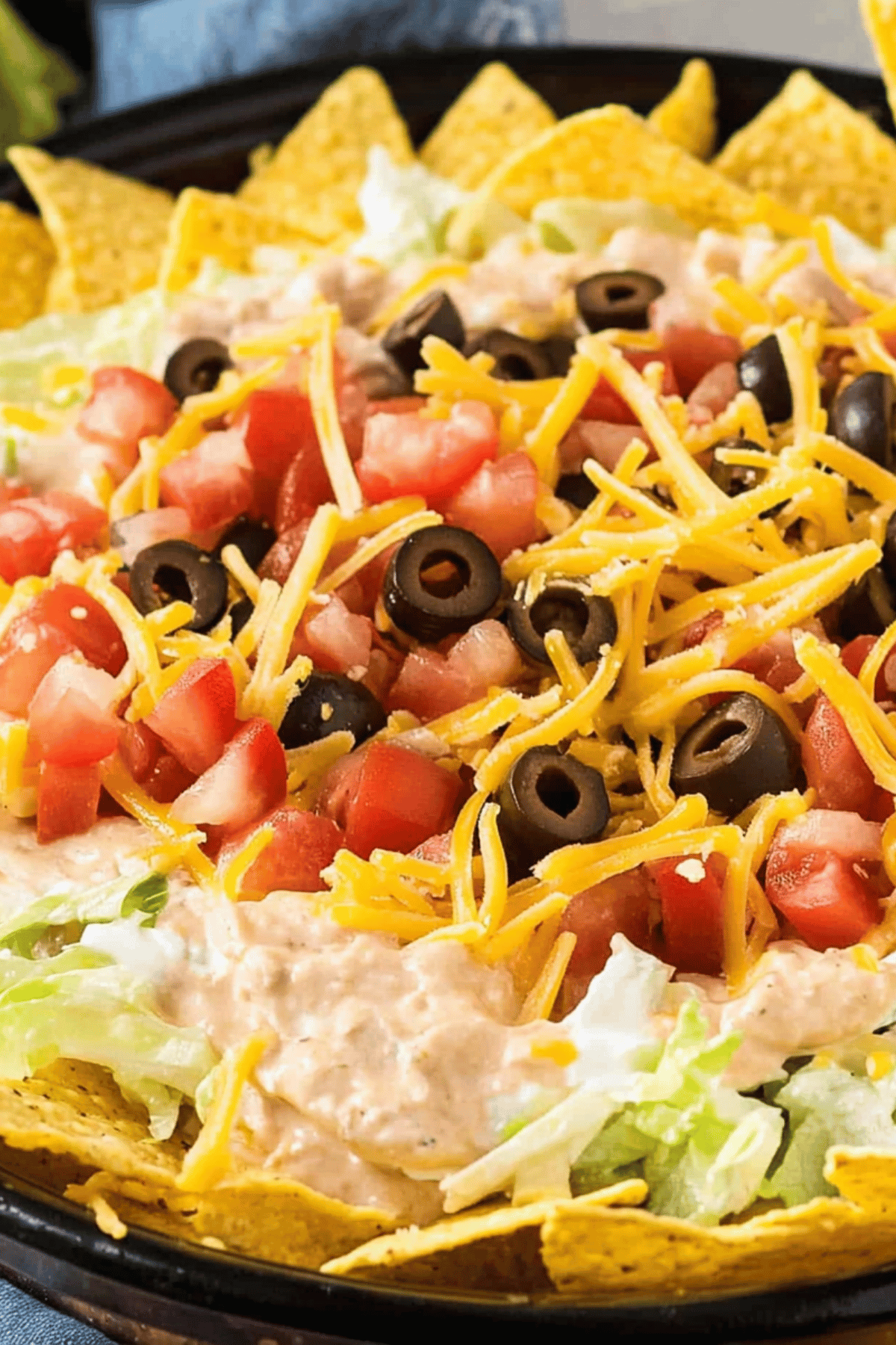 Party-Ready Taco Dip Platter Overhead view of a full platter of taco dip with layers of lettuce, tomatoes, olives, and cheese, surrounded by tortilla chips.