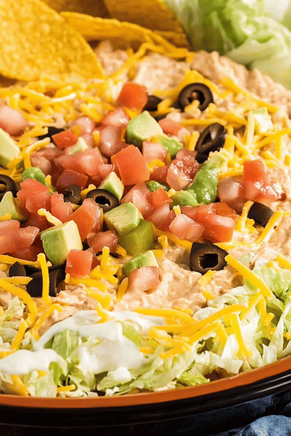 Loaded Taco Dip with Avocado and Sour Cream Taco dip layered with avocado chunks, sour cream, tomatoes, olives, shredded cheese, and lettuce in a round serving dish.